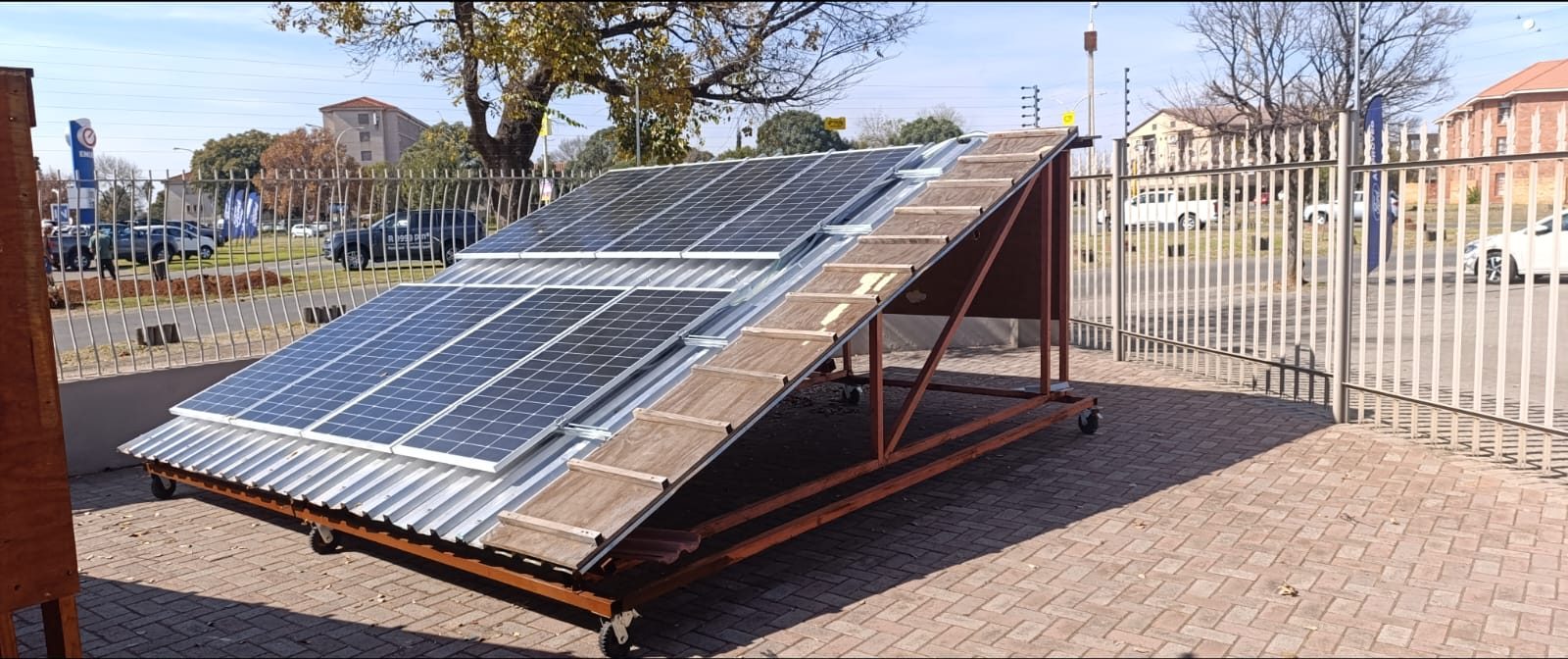 Mobile solar PV training rig with panels on tile and sheet-metal roof sections